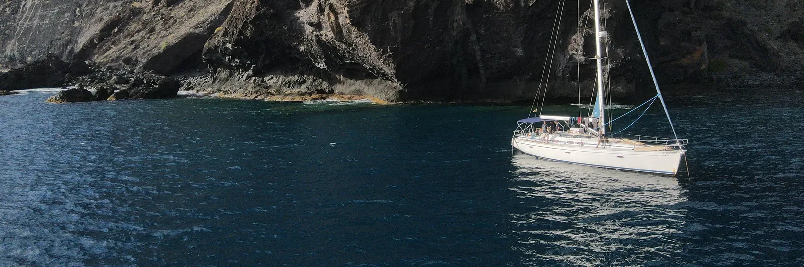 Aerial view of the Picarus sailboat anchored in a cove at the foot of the Los Gigantes cliffs