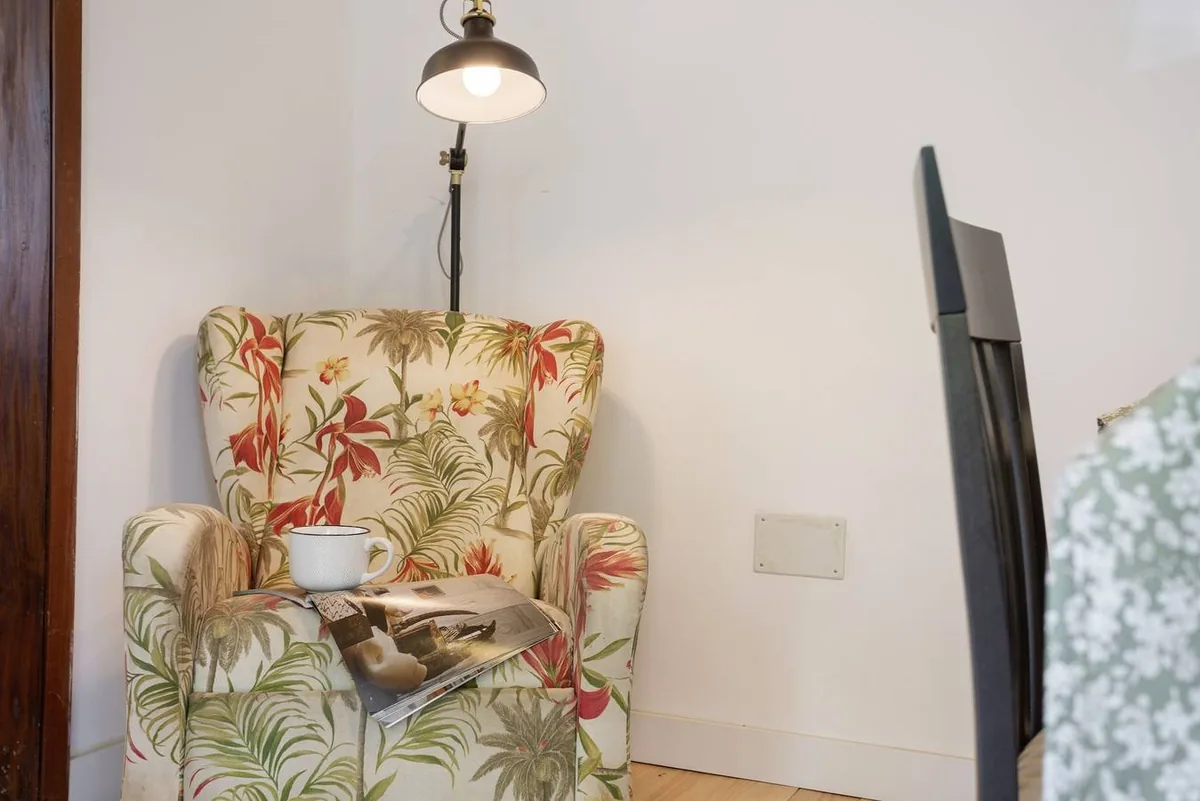 Fauteuil tapissé de motifs floraux avec une tasse de café sur l’accoudoir, sous une lampe de lecture