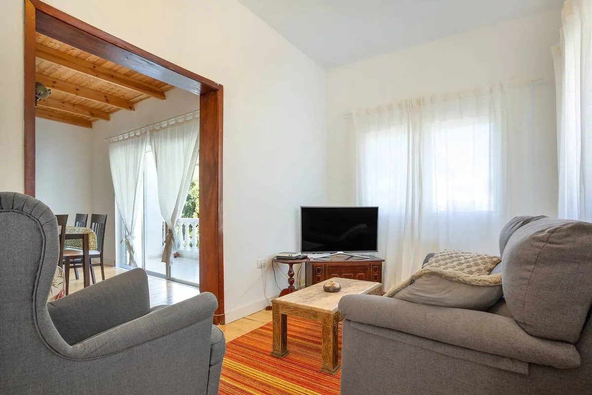 Salon de Picarus Home avec des fauteuils gris, un téléviseur et un passage ouvert vers la salle à manger